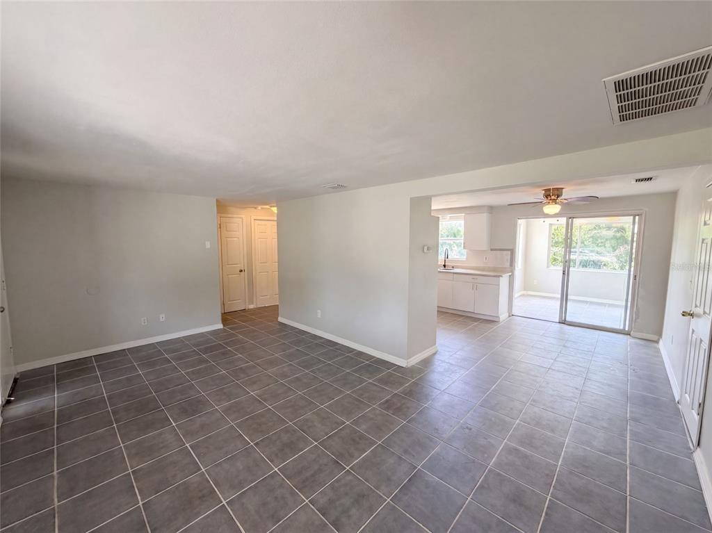 An open-concept living area features gray tile flooring, white walls, and a view into the kitchen — 4718 TRAFFORD ROAD, HOLIDAY, FL