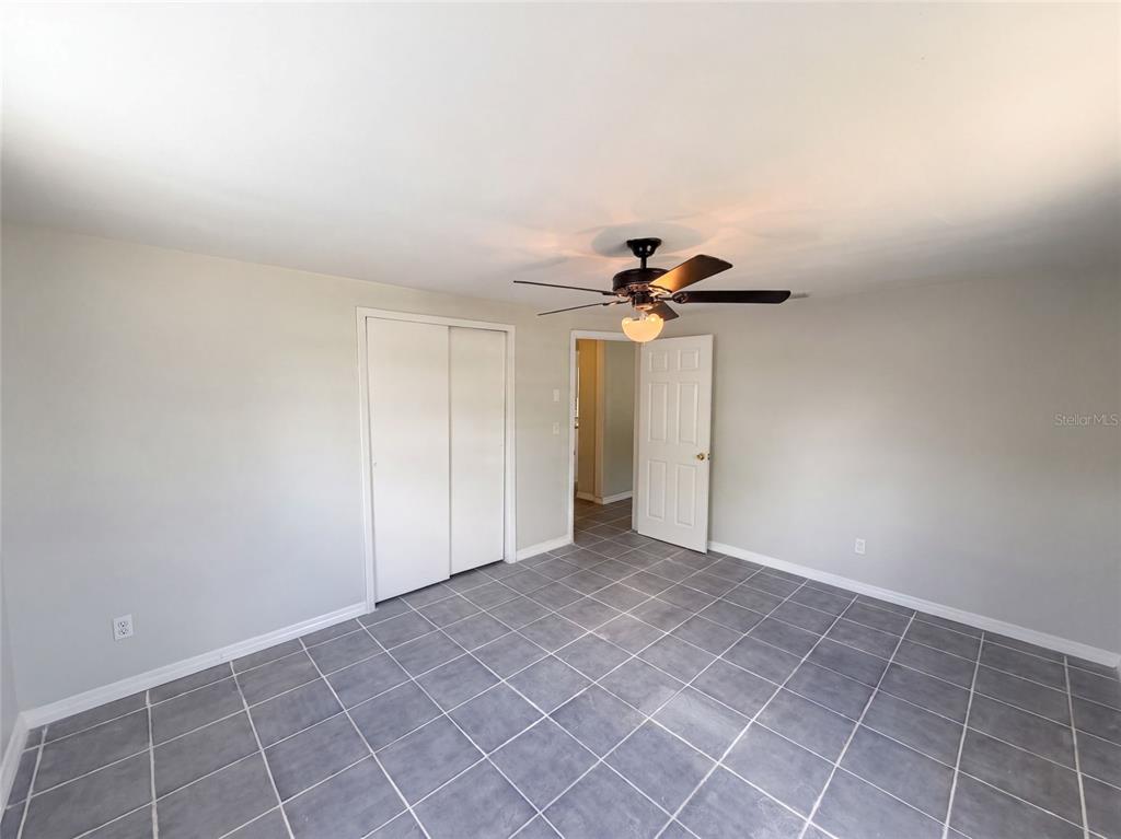 A bedroom with light gray walls, gray tile flooring, a ceiling fan, and white doors — 4718 TRAFFORD ROAD, HOLIDAY, FL
