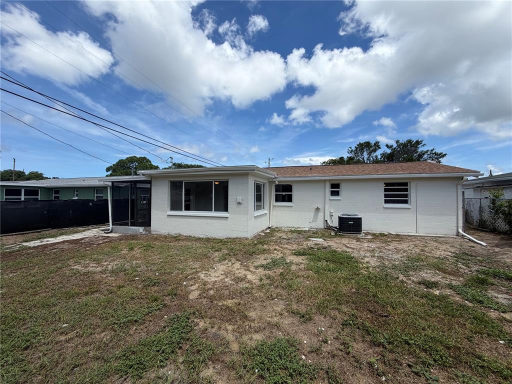 The exterior of a single-story white brick house features a screened porch and backyard — 4718 TRAFFORD ROAD, HOLIDAY, FL