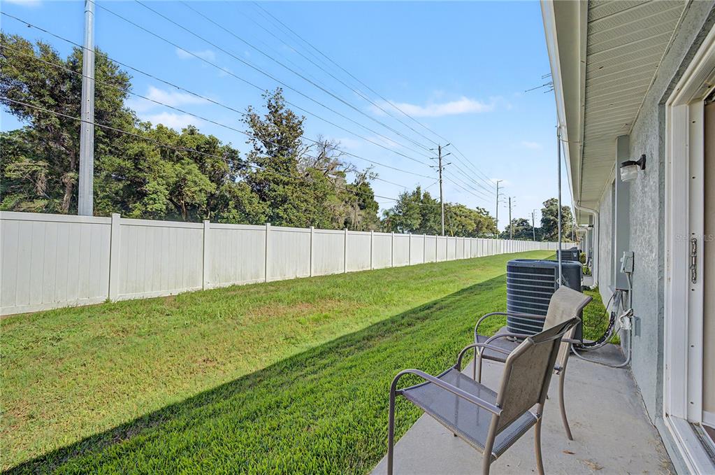 A concrete patio with two chairs sits beside a house next to a long white fence — 6783 BASSWOOD CIRCLE, ZEPHYRHILLS, FL