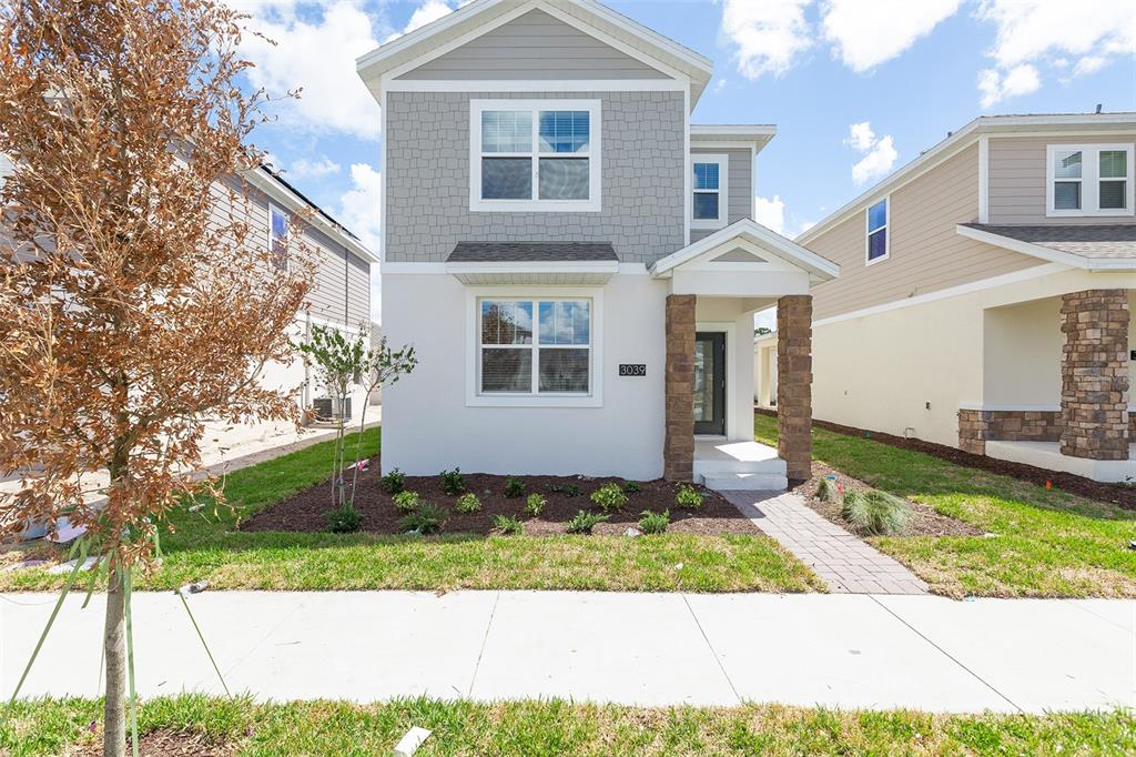 A two-story suburban house features a gray stucco exterior, stone porch pillars, and a walkway — 3039 ADDISON BOULEVARD, ST CLOUD, FL