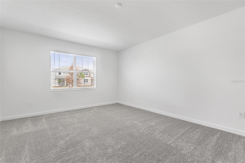 An empty bedroom features white walls, gray carpeting, and a window with blinds — 3039 ADDISON BOULEVARD, ST CLOUD, FL