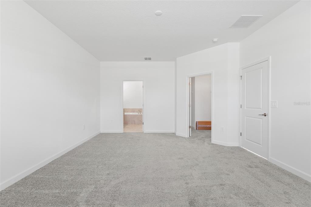 A carpeted bedroom features white walls, two doorways, and a closed white door — 3039 ADDISON BOULEVARD, ST CLOUD, FL