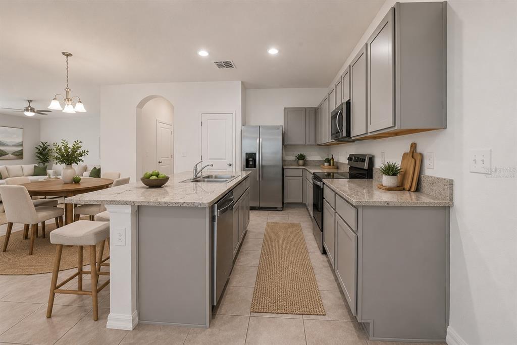 An open-concept kitchen and dining area features gray cabinets, a breakfast bar, and tile flooring — 1574 HUBBELL ROAD, WESLEY CHAPEL, FL