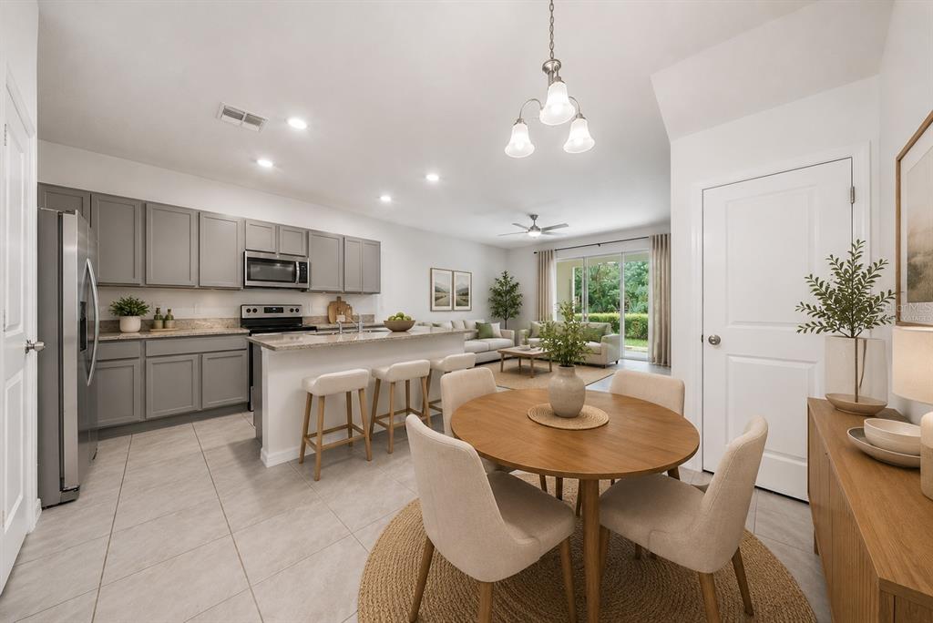 A kitchen with gray cabinets and a granite island opens to a dining area — 1574 HUBBELL ROAD, WESLEY CHAPEL, FL