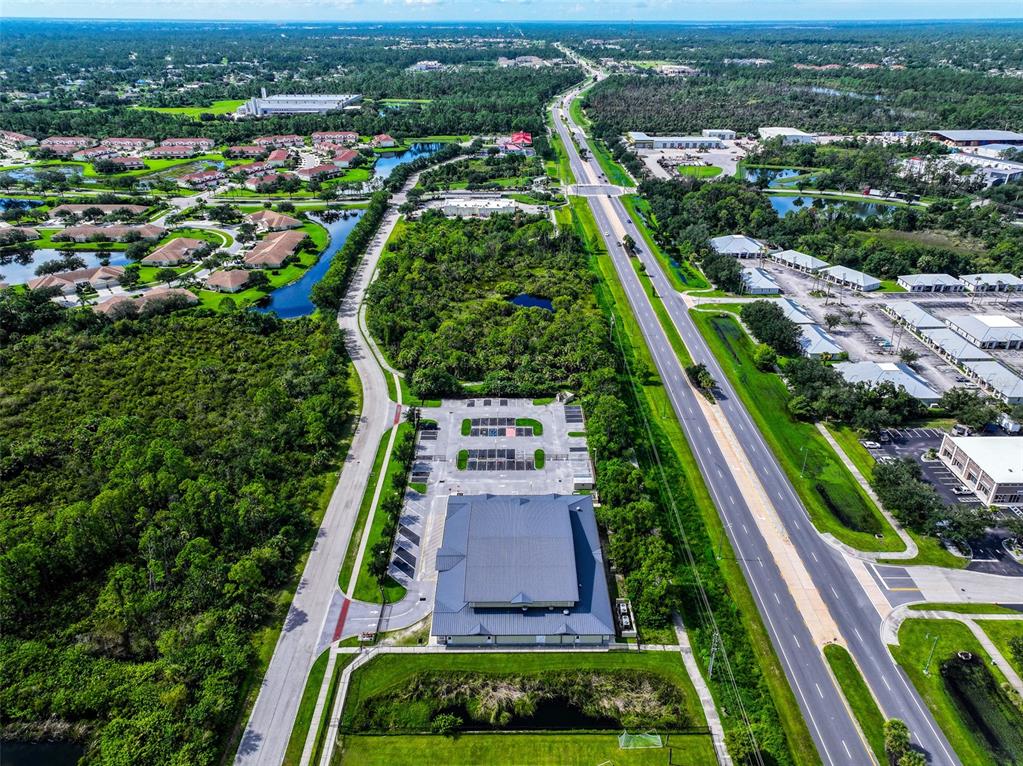 An aerial view shows a commercial building with a parking lot surrounded by dense vegetation — 2597 SYCAMORE STREET, NORTH PORT, FL