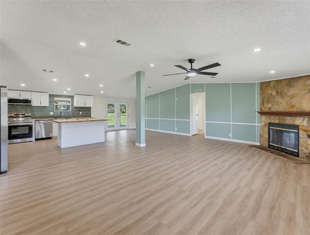 An open-concept living room features light wood flooring, a stone fireplace, and an adjacent kitchen — 11106 FERNWAY LANE, DADE CITY, FL