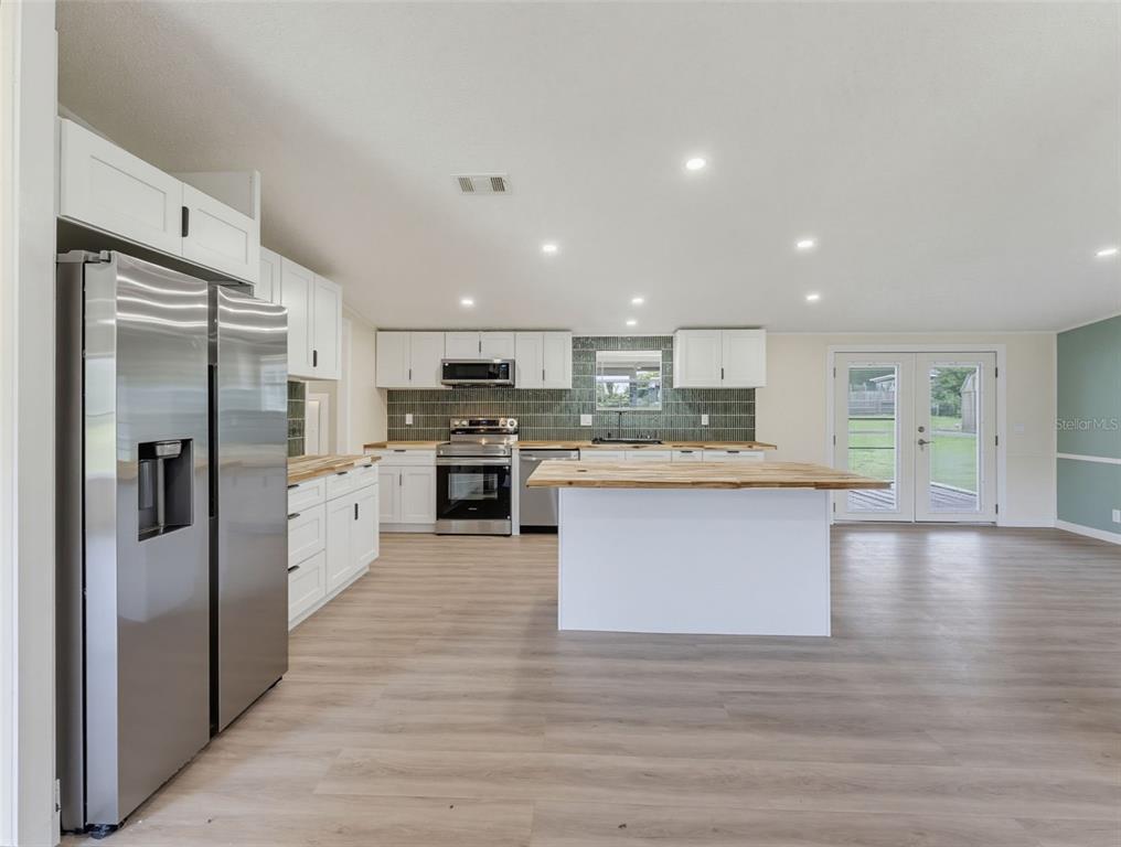 A kitchen features white cabinetry, a wooden island, stainless steel appliances, and a green backsplash — 11106 FERNWAY LANE, DADE CITY, FL