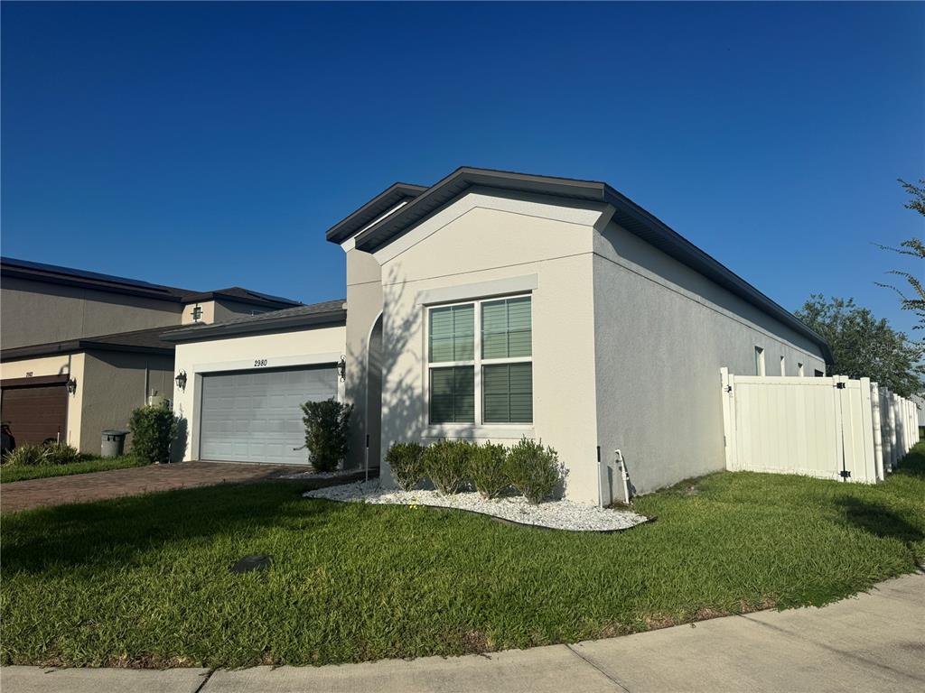 A single-story house with a beige stucco exterior, a two-car garage, and a white fence — 2980 SCARLETT DRIVE, ST CLOUD, FL
