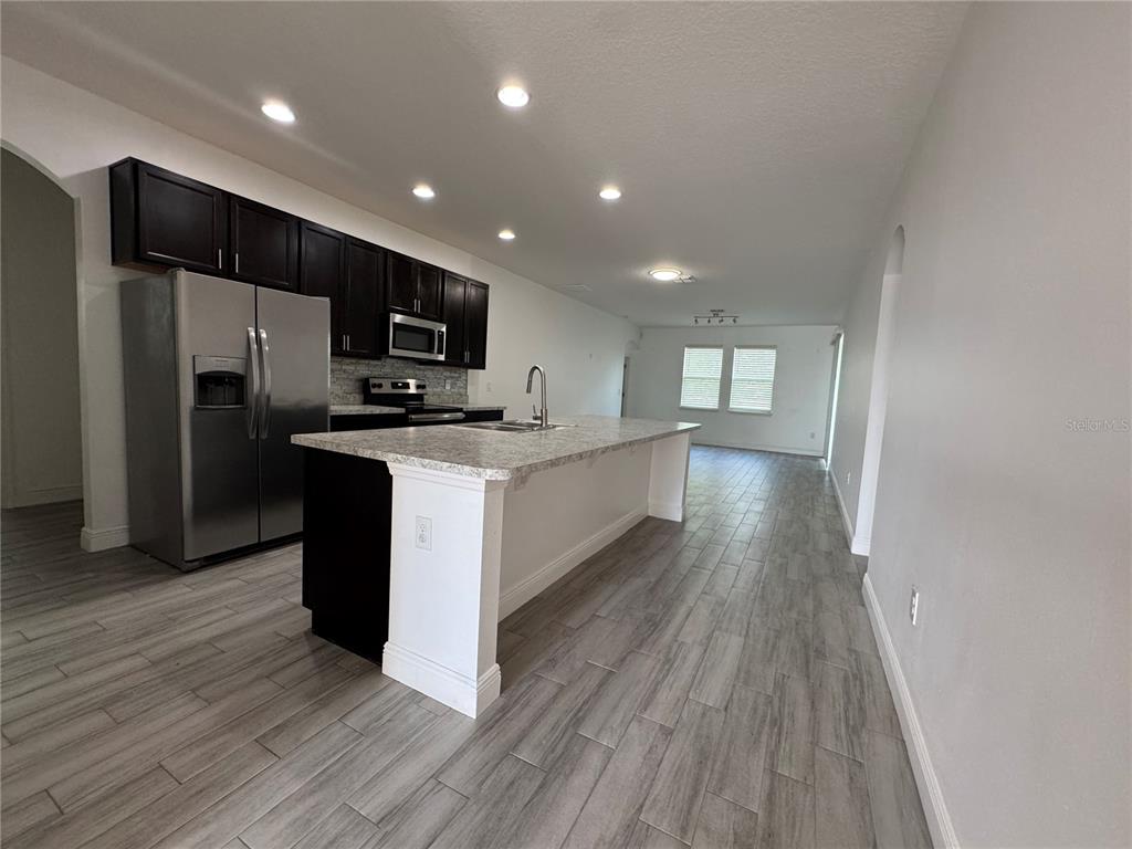 A kitchen features dark cabinets, stainless steel appliances, a granite island, and wood-look tile flooring — 2980 SCARLETT DRIVE, ST CLOUD, FL