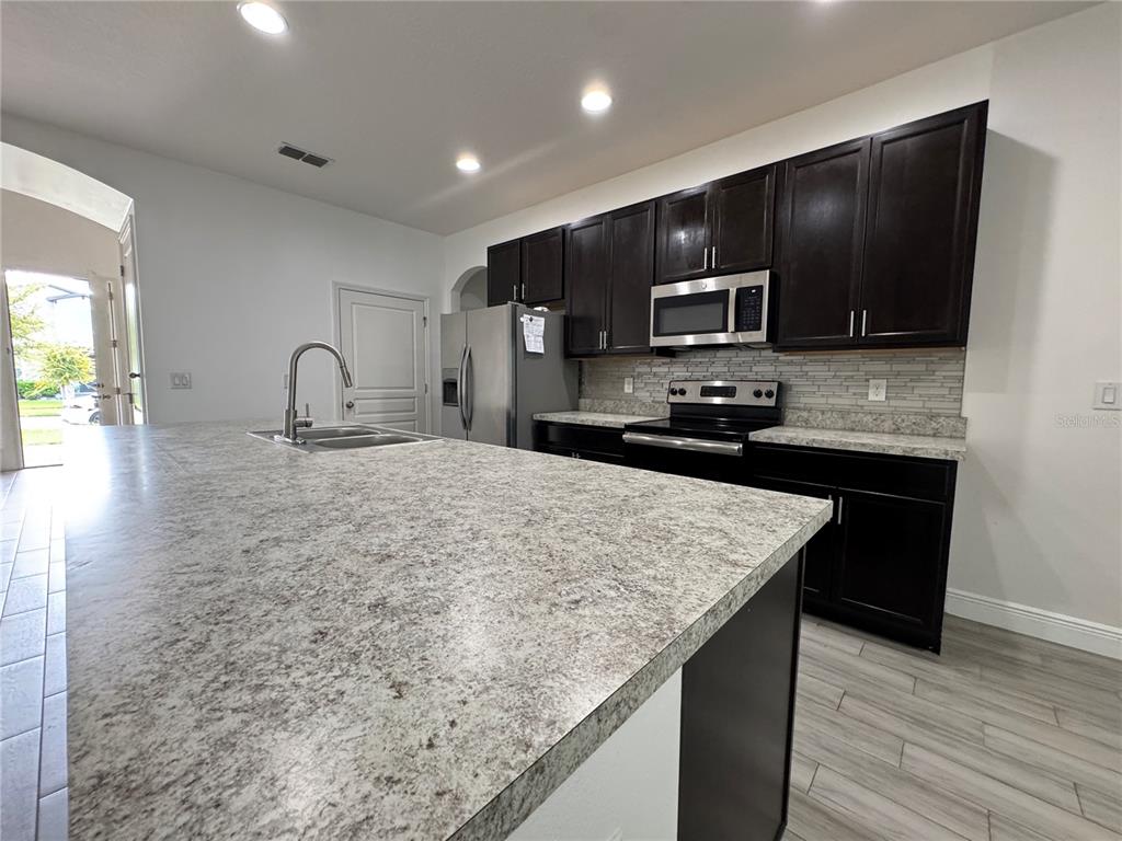 A kitchen features dark wood cabinets, granite countertops, a large island, and stainless steel appliances — 2980 SCARLETT DRIVE, ST CLOUD, FL