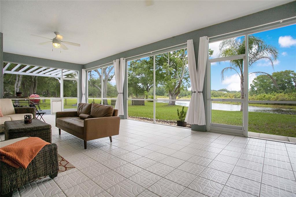 A screened-in porch with tile flooring overlooks a grassy yard and a small pond — 19616 LIVINGSTON AVENUE, LUTZ, FL