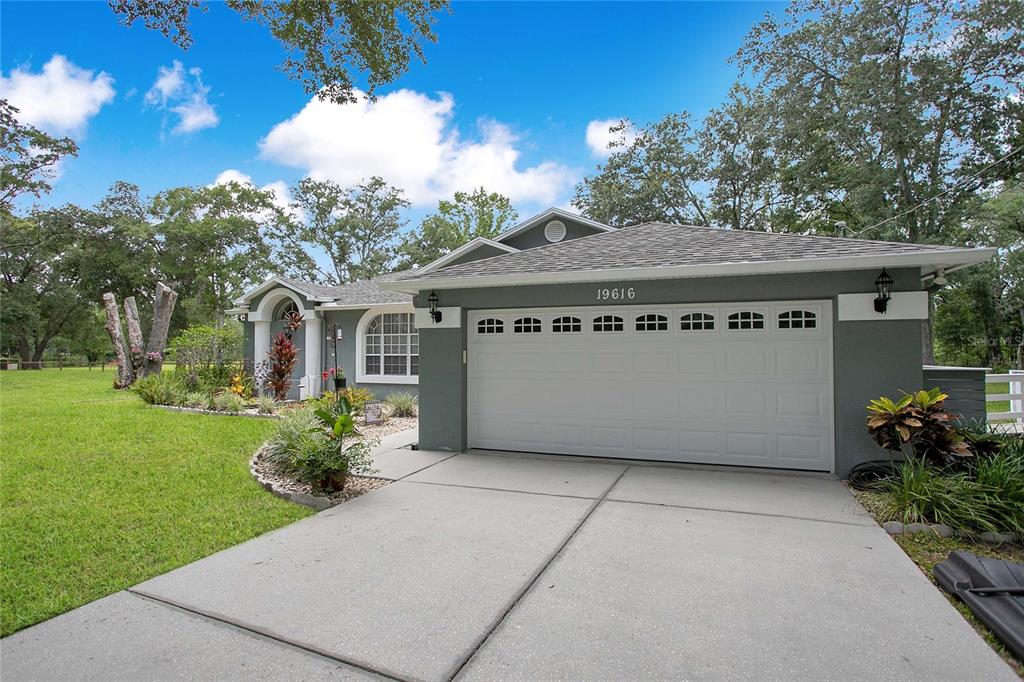 A gray single-story house with a white garage door and a landscaped front yard — 19616 LIVINGSTON AVENUE, LUTZ, FL