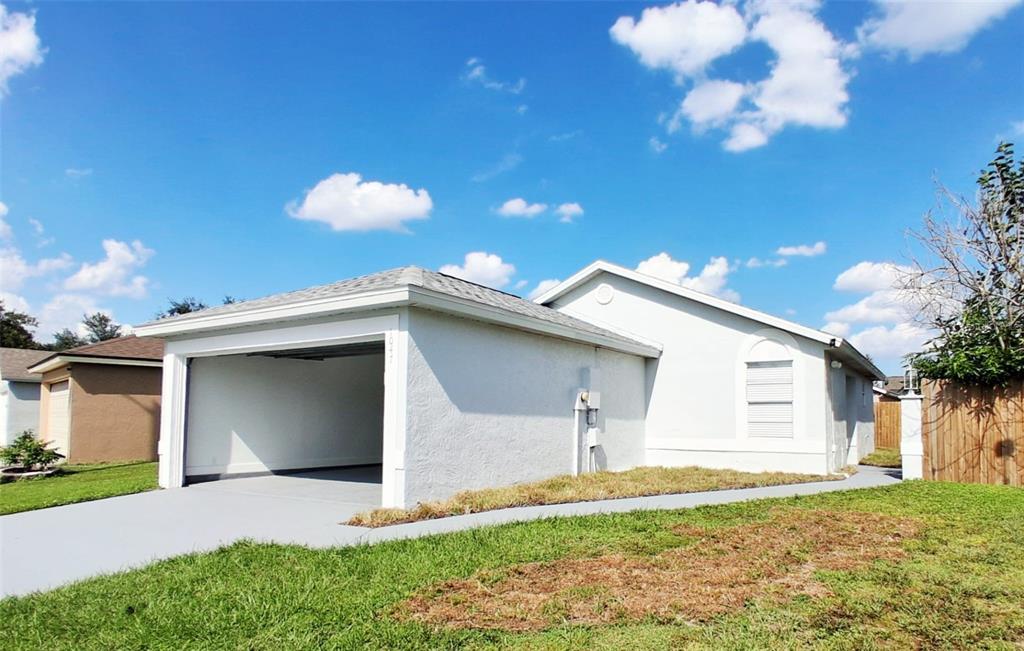 A white stucco house with a side-entry garage and a gray driveway under a blue sky — 1047 FLORIDA HOLLY DRIVE, ORLANDO, FL