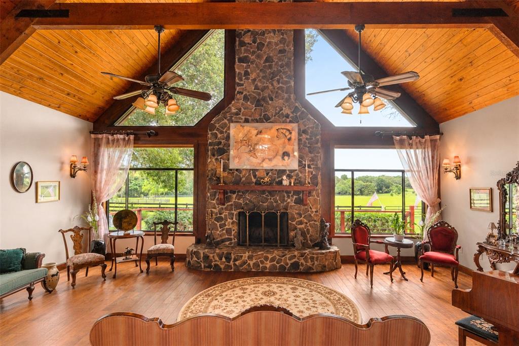 A living room features a stone fireplace, vaulted wood ceilings, and large windows overlooking fields — 35841 TIMBERTOP LANE, FRUITLAND PARK, FL