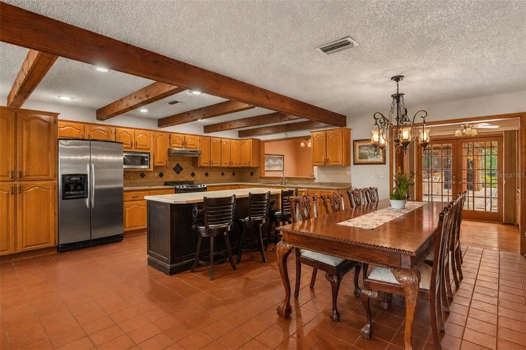 A kitchen and dining area with wood-beam ceilings, wooden cabinets, and terracotta tile flooring — 35841 TIMBERTOP LANE, FRUITLAND PARK, FL