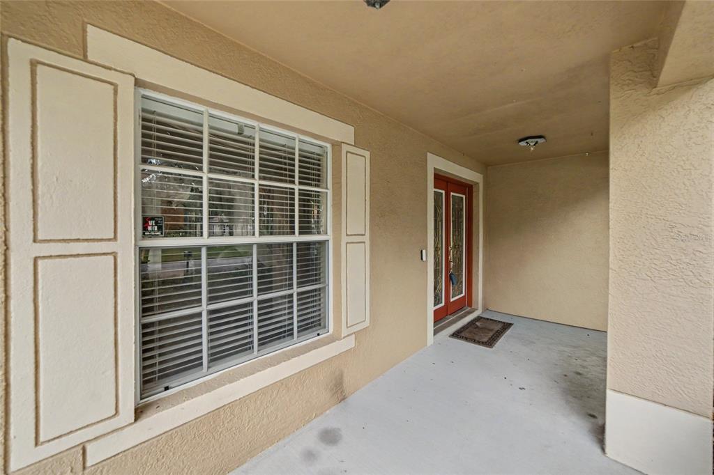 A covered front porch features a window with shutters and a red front door — 15110 HERONGLEN DRIVE, LITHIA, FL