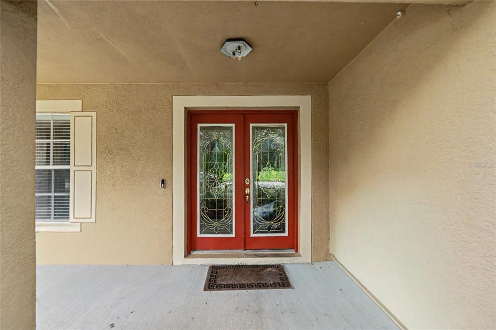 A covered porch features a red double front door with decorative glass inserts and shutters — 15110 HERONGLEN DRIVE, LITHIA, FL
