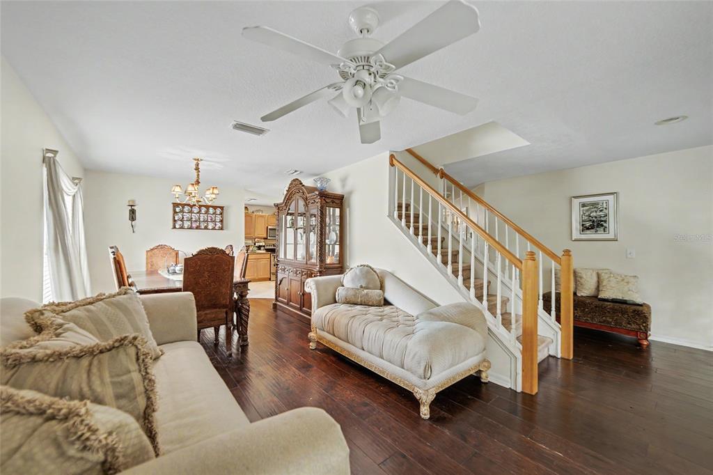A living and dining room area features dark wood floors, a staircase, and a ceiling fan — 15110 HERONGLEN DRIVE, LITHIA, FL