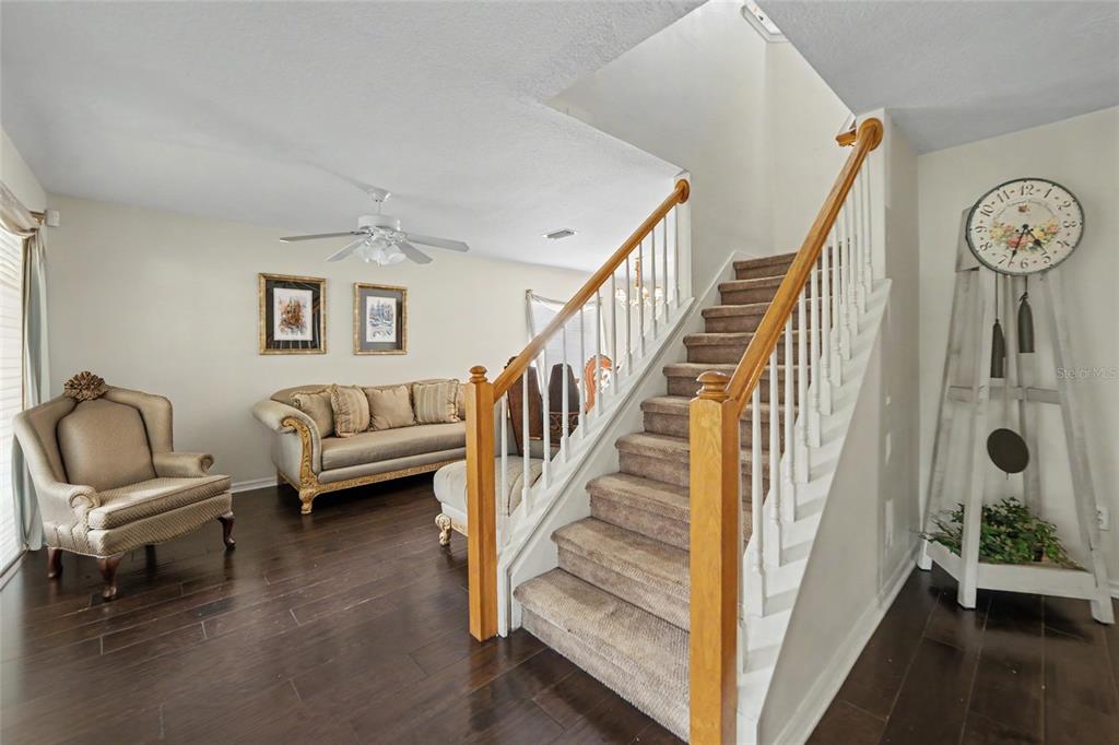 A living room features dark wood floors, a carpeted staircase, and a decorative floor clock — 15110 HERONGLEN DRIVE, LITHIA, FL