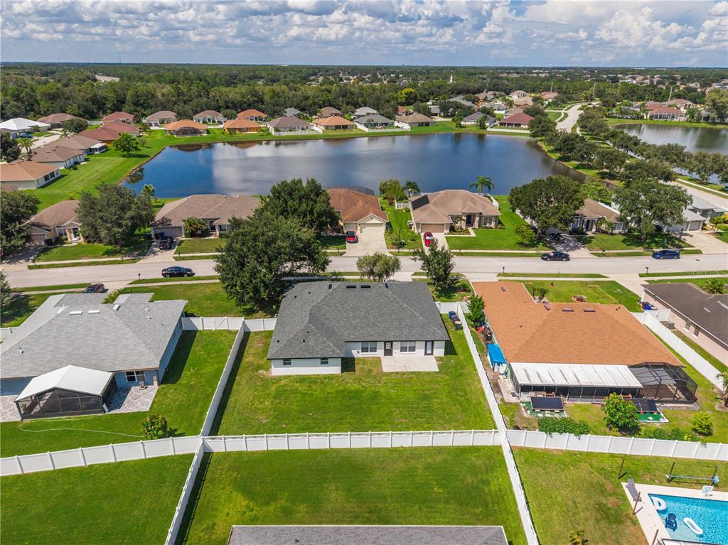 An aerial view shows a suburban neighborhood with houses, a central lake, and fenced backyards — 3207 SLATE ROAD, ST CLOUD, FL