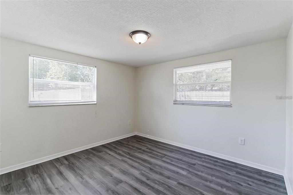 An empty bedroom features light-colored walls, gray wood-look flooring, and two windows with blinds — 403 PINEWOOD AVENUE, NOKOMIS, FL
