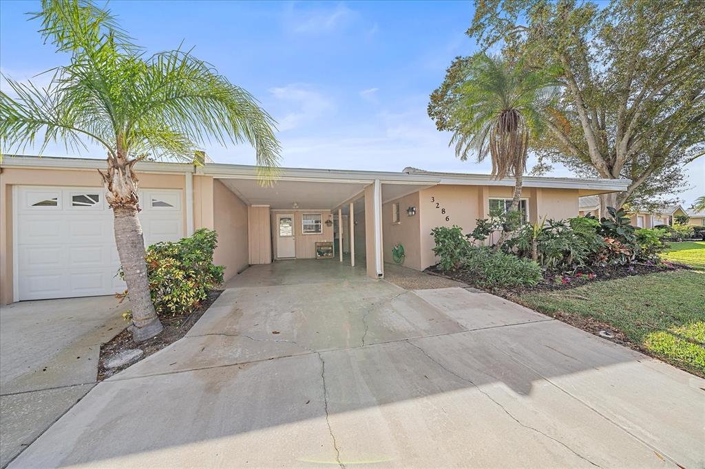 A single-story house exterior features a concrete driveway, a carport, and a palm tree — 3286 BRUNSWICK LANE UNIT 704, SARASOTA, FL