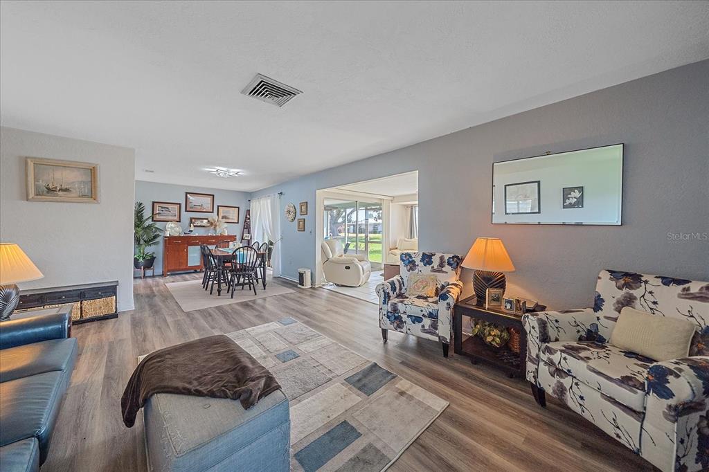 A living room with wood-look flooring, a dark leather sofa, and a floral armchair — 3286 BRUNSWICK LANE UNIT 704, SARASOTA, FL