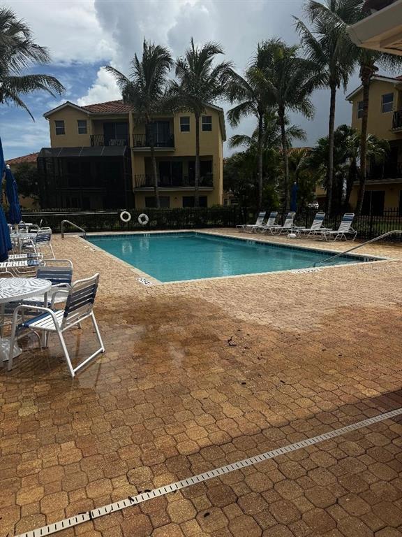A swimming pool sits on a paved patio surrounded by palm trees and apartment buildings — 1205 3RD ST CIRCLE E, PALMETTO, FL