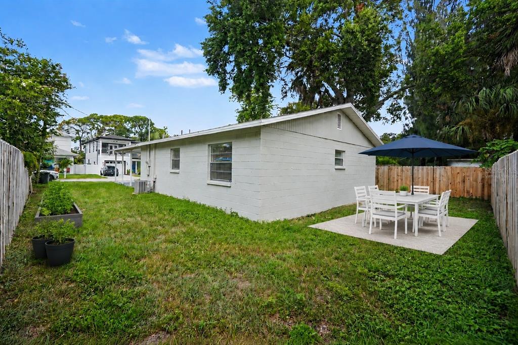 The exterior of a white concrete block house features a backyard patio with dining furniture — 5733 66TH LANE N, ST PETERSBURG, FL