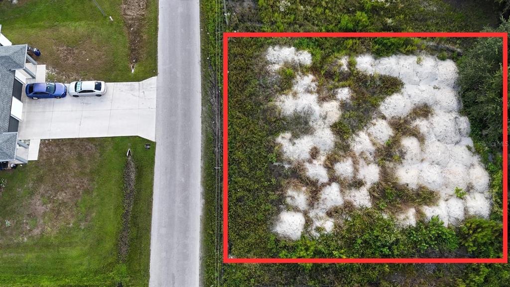 An aerial view shows a vacant, rectangular lot marked with a red border beside a road — 4427 24TH STREET SW, LEHIGH ACRES, FL