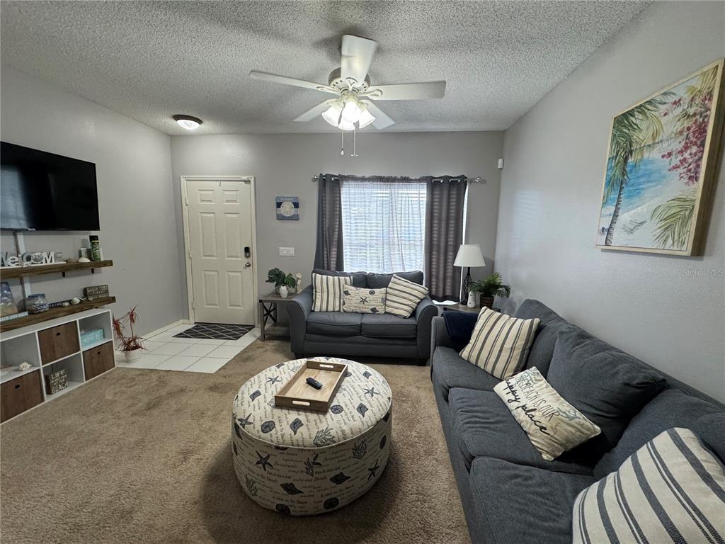 A living room features a gray sofa, a round patterned ottoman, and a television console — 4540 RUNABOUT WAY, BRADENTON, FL
