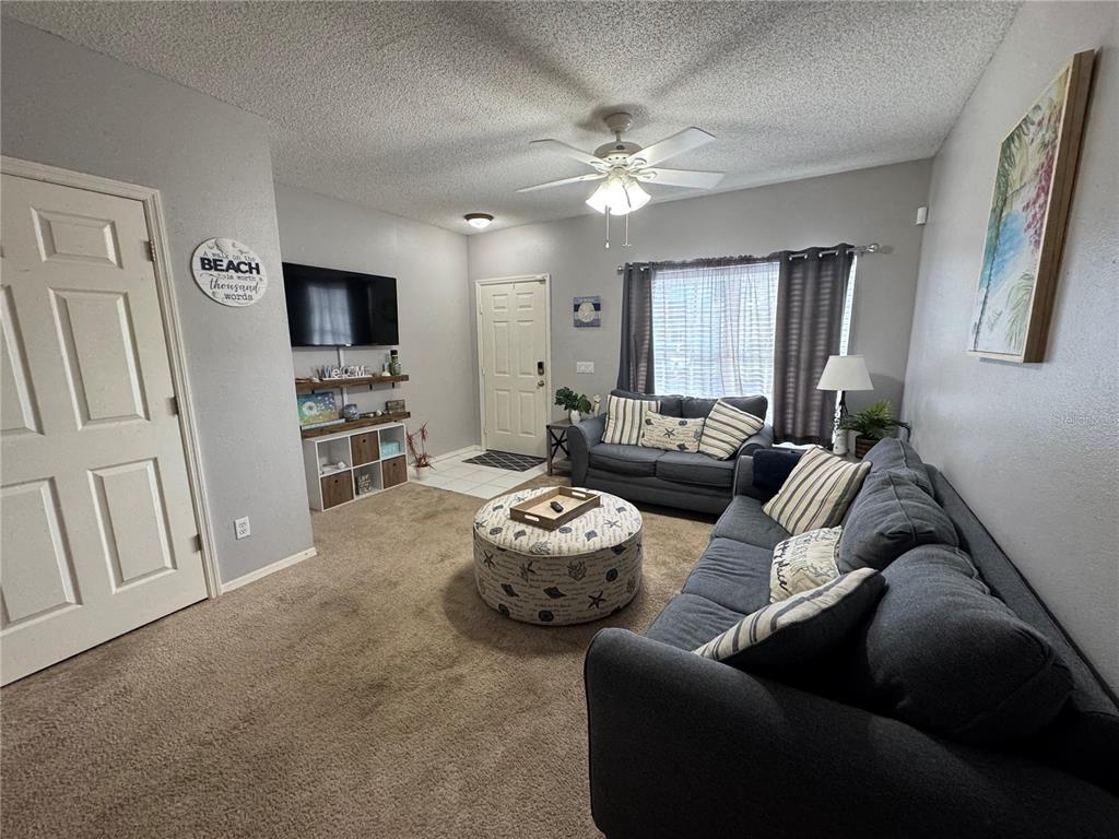 A living room features gray sofas, a round patterned ottoman, and a wall-mounted television — 4540 RUNABOUT WAY, BRADENTON, FL