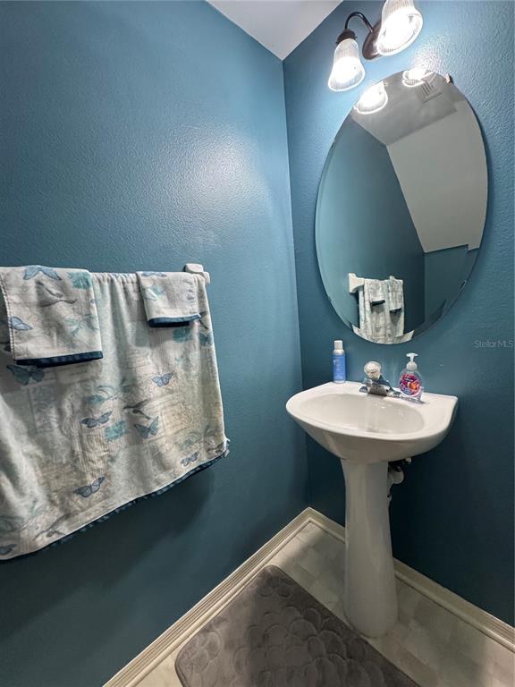 A small bathroom features a pedestal sink, an oval mirror, and blue walls — 4540 RUNABOUT WAY, BRADENTON, FL