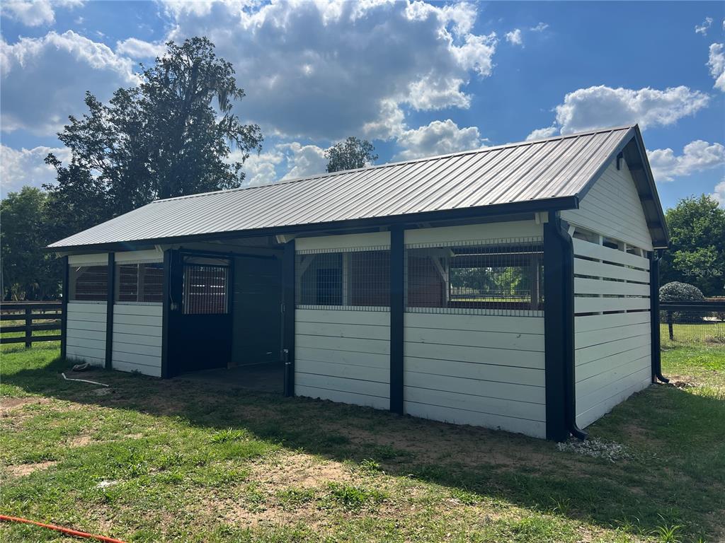 A white horse barn with a metal roof stands in a grassy field — 1575 NE 100TH STREET, ANTHONY, FL