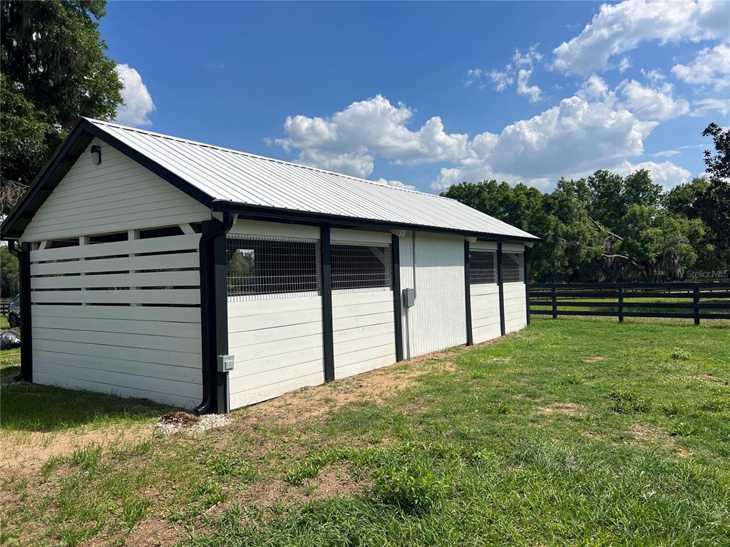 A white, metal-roofed horse barn stands in a grassy field with black trim and fencing — 1575 NE 100TH STREET, ANTHONY, FL