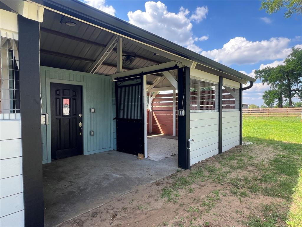 A covered patio area features a black door, a sliding stall gate, and white siding — 1575 NE 100TH STREET, ANTHONY, FL