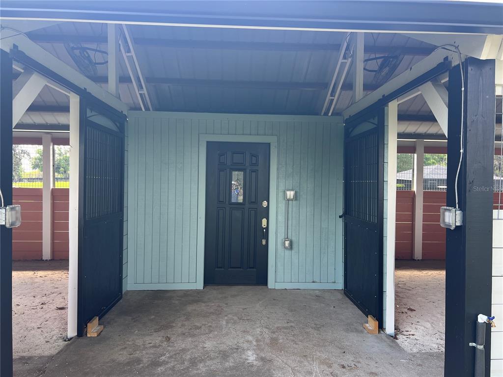 A covered walkway leads to a dark door flanked by open black metal stall gates — 1575 NE 100TH STREET, ANTHONY, FL