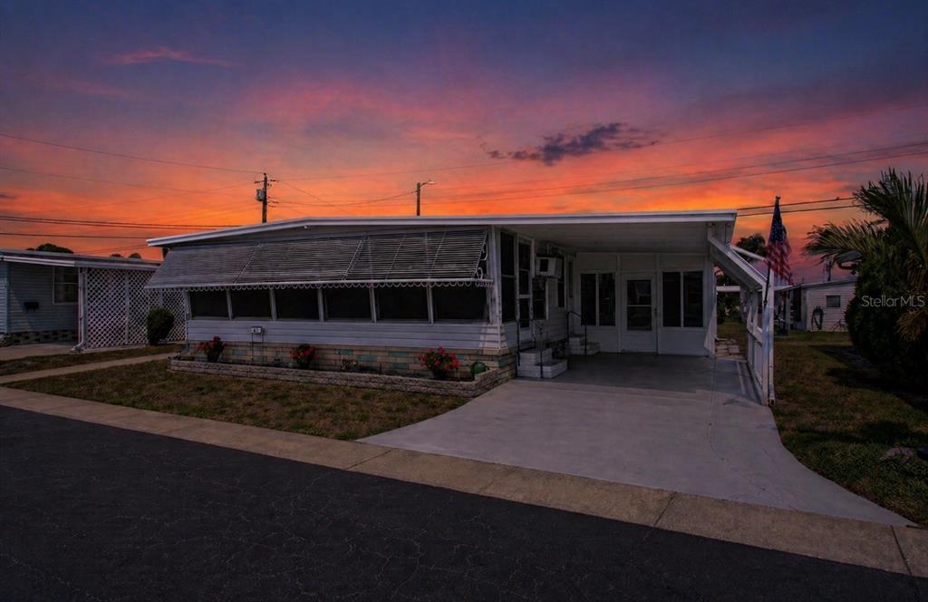 A single-story mobile home with a carport and screened-in porch at sunset — 2000 E BAY DRIVE UNIT 85, LARGO, FL