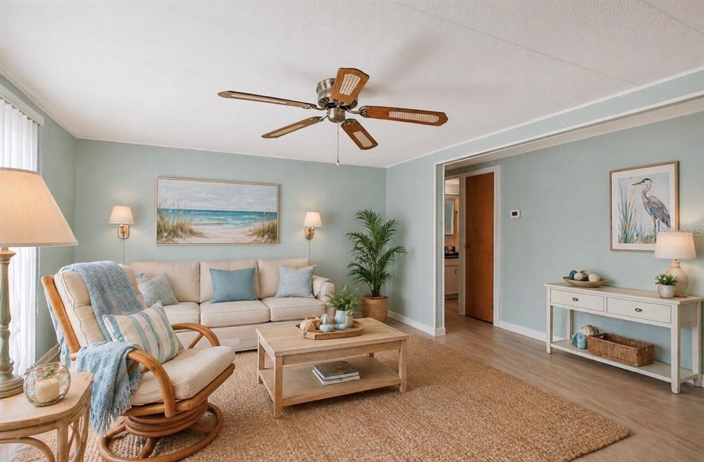 A living room features light blue walls, a beige sofa, a rattan chair, and a ceiling fan — 2000 E BAY DRIVE UNIT 85, LARGO, FL