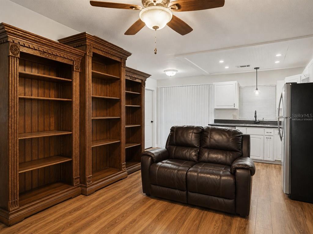 A living area features wood-look flooring, large wooden bookshelves, and a brown leather loveseat — 2508 AVENUE A SW, WINTER HAVEN, FL