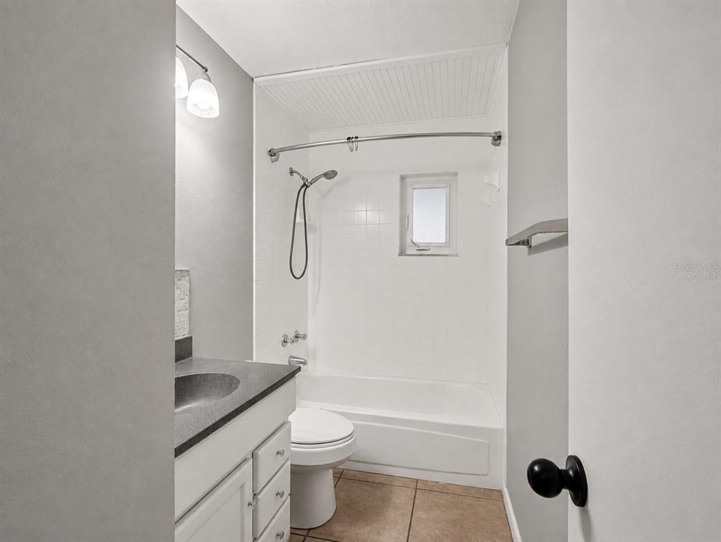 A bathroom features a white tub-shower combo, a vanity with a dark countertop, and tile flooring — 2508 AVENUE A SW, WINTER HAVEN, FL