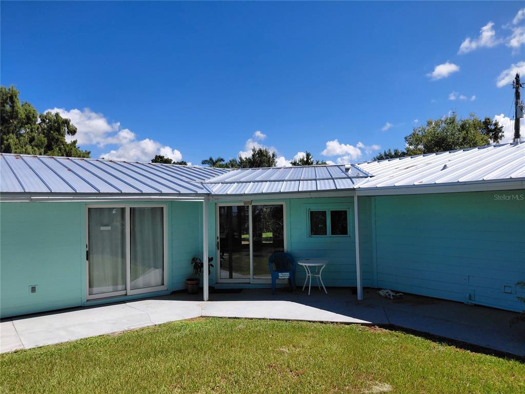 A light blue house exterior features a metal roof, sliding glass doors, and a concrete patio — 1303 CLUB LANE, LORIDA, FL