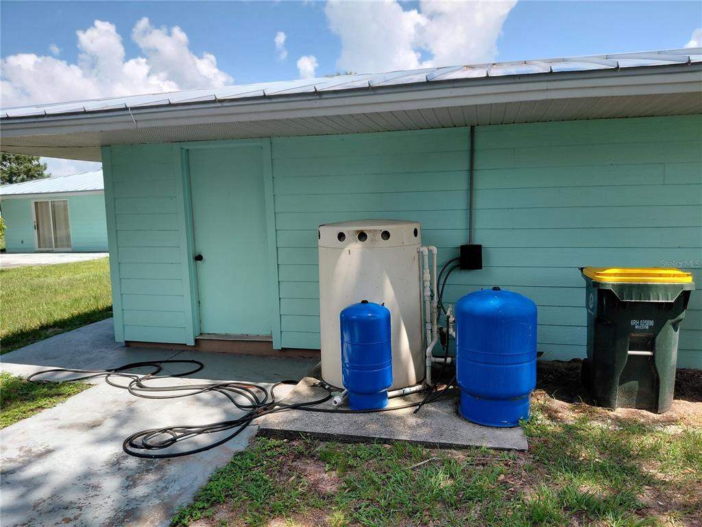 The exterior of a light blue house features a water treatment system and a trash bin — 1303 CLUB LANE, LORIDA, FL