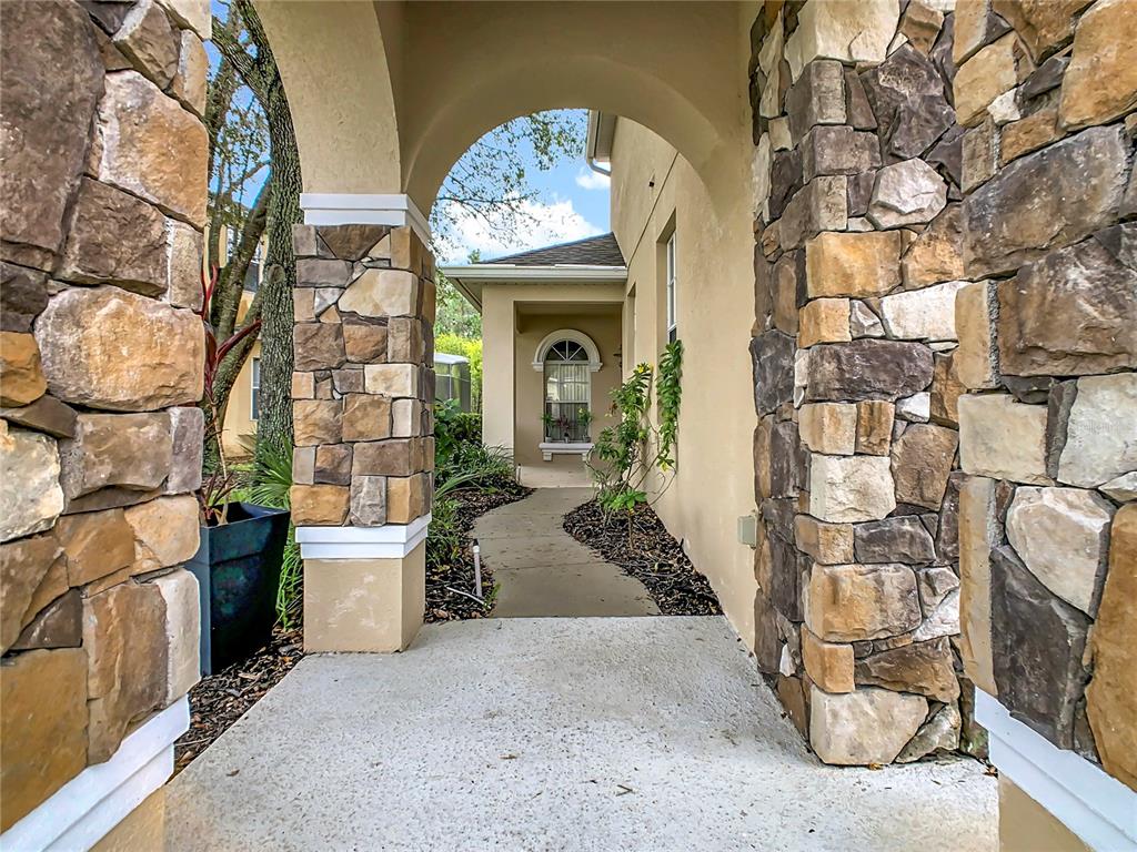 A stone-columned arched entryway leads to a concrete walkway alongside a stucco house — 574 TUPELO CIRCLE, DAVENPORT, FL
