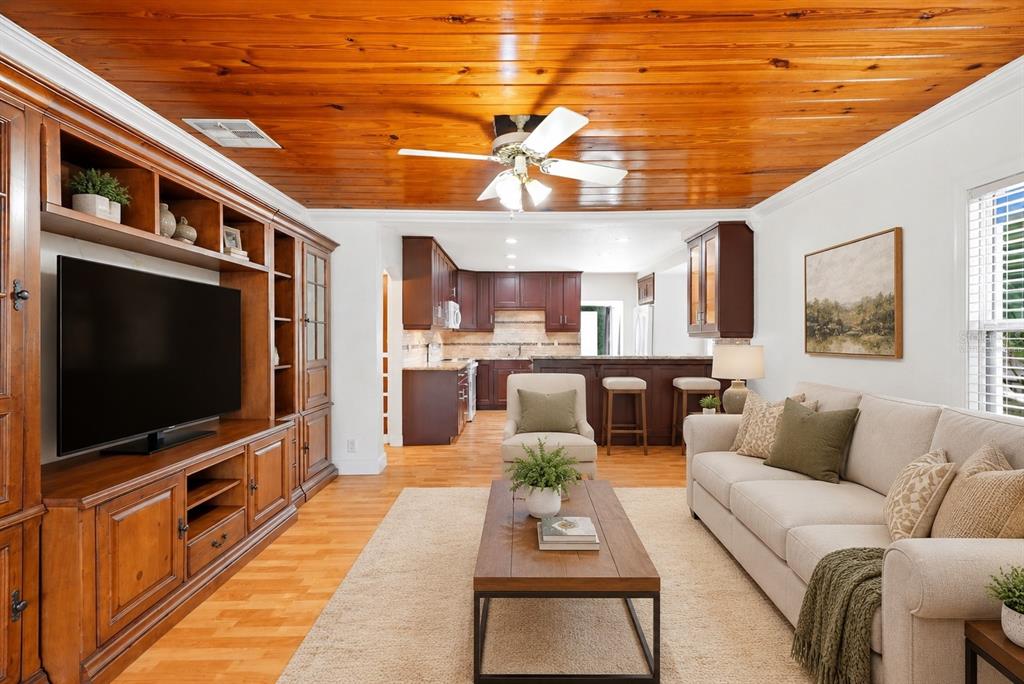 A living room with a wood-paneled ceiling, built-in entertainment center, and an open kitchen beyond — 3620 BURLINGTON AVENUE N, ST PETERSBURG, FL