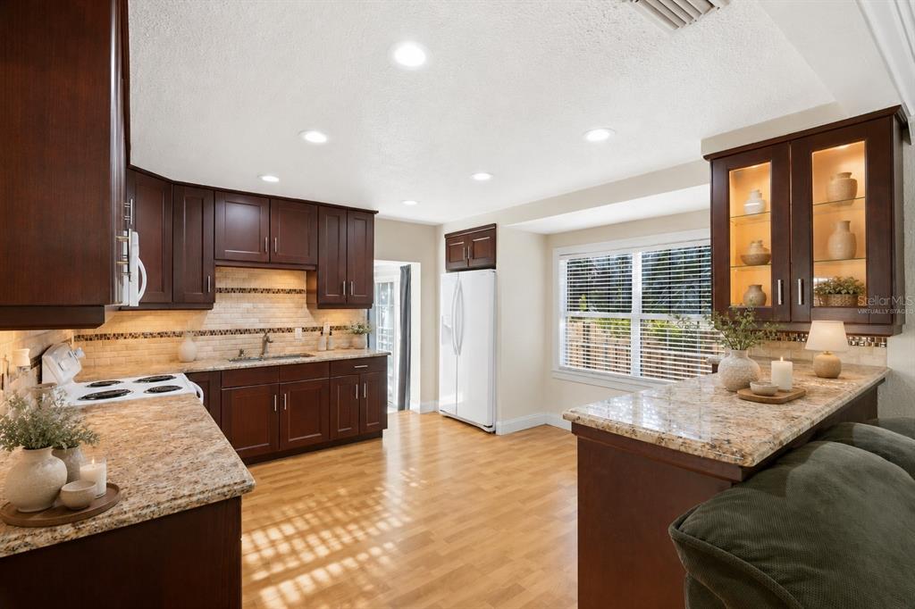 A kitchen with dark wood cabinets, granite countertops, light wood flooring, and a white refrigerator — 3620 BURLINGTON AVENUE N, ST PETERSBURG, FL