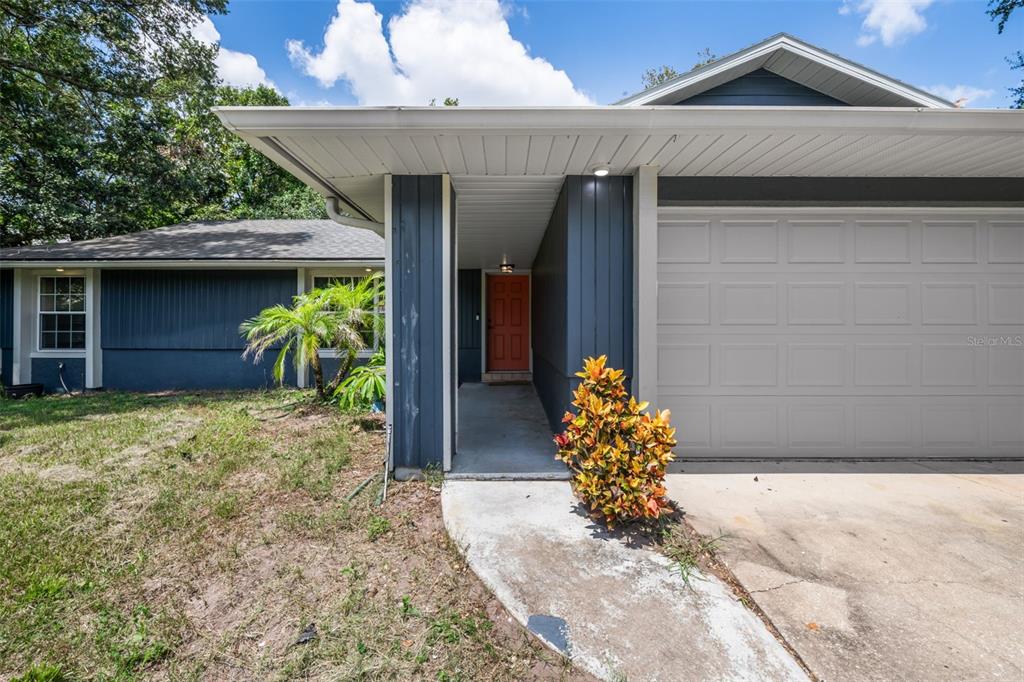 A blue house exterior features a concrete walkway leading to an orange front door — 2380 PEMBERTON STREET, OVIEDO, FL