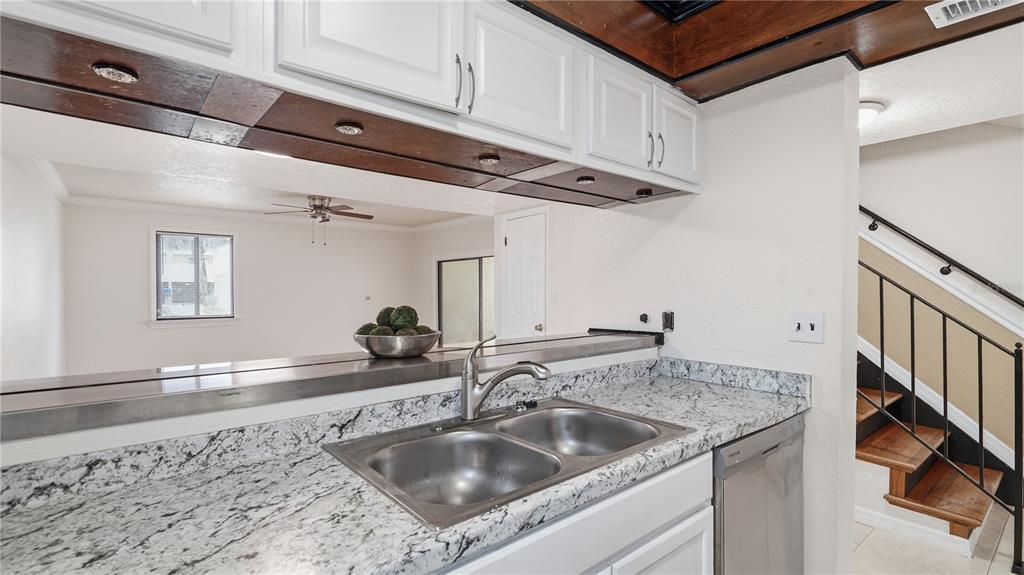 A kitchen with granite countertops, a double sink, and white cabinets overlooking a living area — 1412 OAK PLACE UNIT A, APOPKA, FL