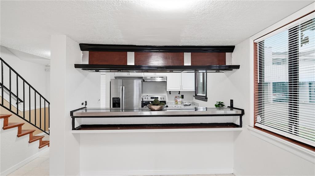 A kitchen pass-through window with a dark wood valance overlooks a white-walled dining area — 1412 OAK PLACE UNIT A, APOPKA, FL